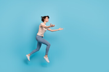Fototapeta na wymiar Full length photo of sweet funny lady dressed beige t-shirt jumping high catching arms empty space isolated blue color background