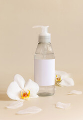 One pump dispenser bottle near white orchid flowers on light yellow close up. Mockup