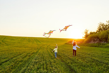 Smiling girl and brother boy running with flying colorful kites on the high grass meadow. Happy...