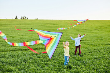 Smiling girl and brother boy running with flying colorful kites on the high grass meadow. Happy...