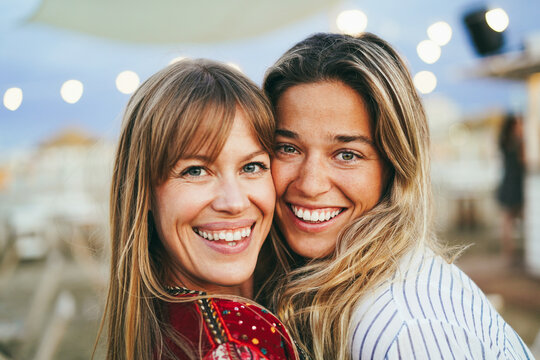 Young female friends smiling on camera with beach bar on background - Focus on right girl face