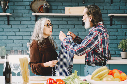Senior couple putting on aprons before preparing food in kitchen