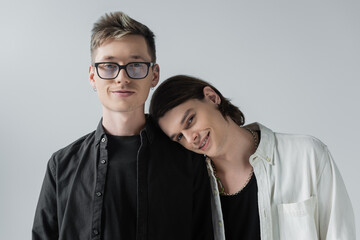 Smiling gay couple looking at camera isolated on grey.