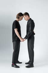 Side view of young gay couple holding hands on grey background.