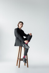 Full length of stylish man sitting on chair on grey background.