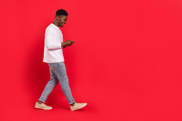 Full size profile portrait of cheerful person walk use telephone chatting isolated on red color...