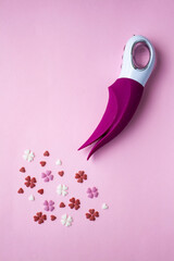 Pink vibrator with a white handle toy for adults lies on a pink background, near the decorative hearts mimic an orgasm. Conceptual photo.