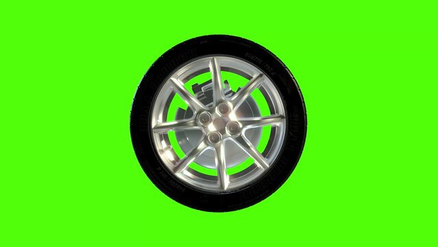 Side on view of a 3D wheel rolling across the screen. Standard black, rubber tyre and wheel rim in a continuous spin. Footage with a green screen for isolating the object.