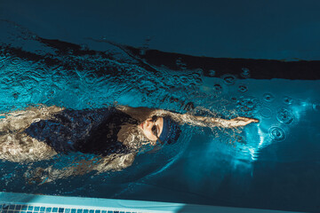 High angle of professional sportswoman in goggles and swimsuit swimming in backstroke or back crawl...