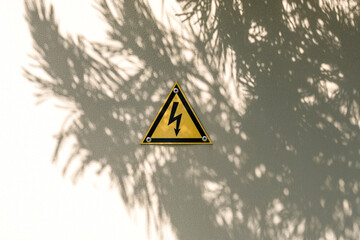 High voltage yellow triangle warning sign on gray metal doors with tree shadow