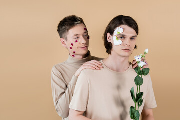 Young man with petals on face hugging partner with eustoma isolated on beige.