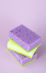 Three colored sponges for washing dishes and other domestic needs on purple background. Vertical. Close-up.Top view. Copy space for your text..
