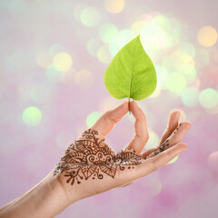Woman with henna tattoo on palm holding green leaf against blurred lights, bokeh effect
