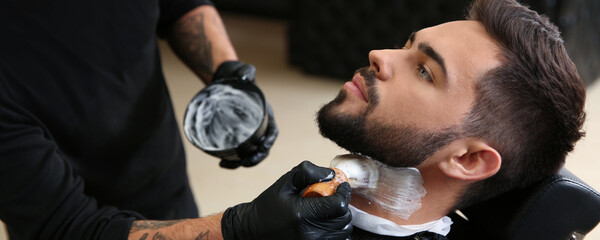 Professional hairdresser applying shaving foam onto client's skin in barbershop. Banner design