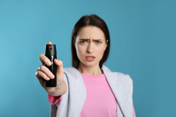 Young woman using pepper spray on light blue background