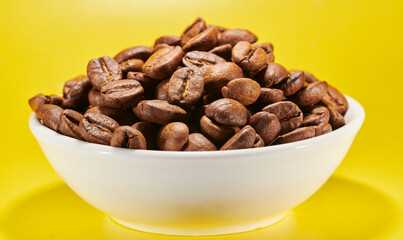 Roasted coffee beans in bowl isolated close up on yellow background, clipping path