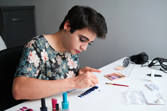 Young gender fluid person in a dress painting false nails with glitter nail polish.