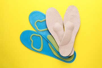 LIght blue and beige orthopedic insoles on yellow background, flat lay