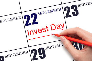 Hand drawing red line and writing the text Invest Day on calendar date September 22. Business and financial concept.