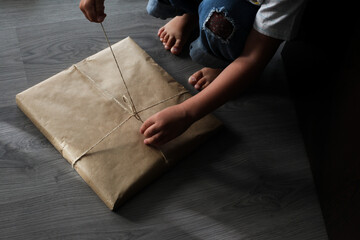 Child unpacks a gift. Kid hands untie the rope. Craft paper present unpacking
