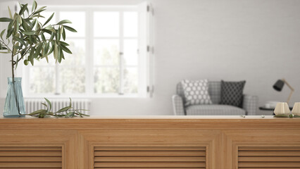 Wooden table top, cabinet, panel or shelf with shutters close up. Olive branch in vase and candles. Blurred background with white living room with armchair and window, interior design