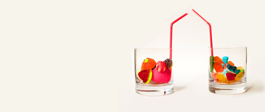 Jelly sugar candies in two glasses with drinking straw on white background with copy space
