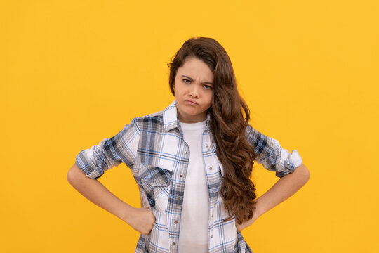 angry teen child in checkered shirt with long curly hair on yellow background