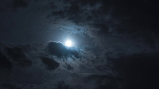 Mysterious night sky with clouds in the moonlight from the full moon. Nighttime Timelapse