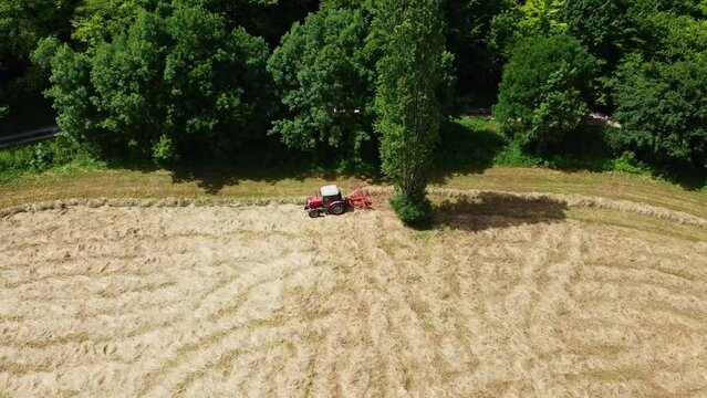 Tracteur vu de profil en train de faire l'andain gr&acirc;ce &agrave; une petite machine agricole. Andainage en bordure de for&ecirc;t.