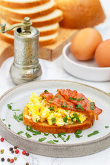 Bread toast with scrambled eggs, fried bacon and parsley close-up in a gray plate on a marble background. Delicious breakfast. Brunch. Selective focus