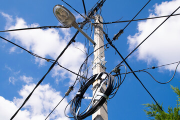 High voltage electricity pole, street lamp and blue sky with white clouds.
