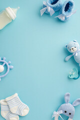 Fototapeta na wymiar Baby boy concept. Top view vertical photo of booties socks soother teddy bear toy teether milk bottle and knitted bunny rattle toy on isolated pastel blue background with empty space in the middle