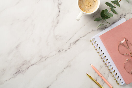 Business concept. Top view photo of workspace pink planners stylish glasses cup of coffee pens and eucalyptus on white marble background with copyspace