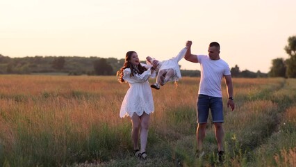 Parents have a fun, play and lift up by the hands their daughter on meadow.