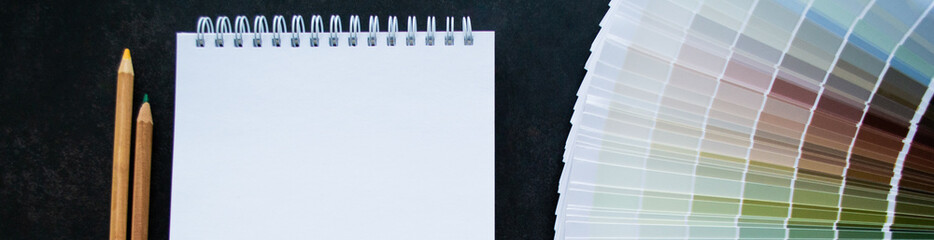 Banner with fan paint samples interior design painting. Multicolored natural colors. Black background, White notebook for copy space and pencils