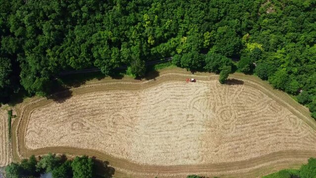 Champ de foin vu du ciel, entour&eacute; de vastes for&ecirc;ts. Vue a&eacute;rienne d'un tracteur en pleine nature.