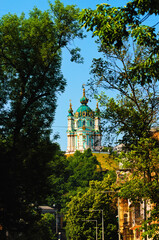 Saint Andrew's Church on the top of green hill. Tree leaves border. Natural frame. Blue sky...