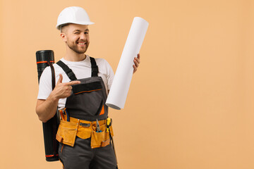 Positive construction engineer examines a drawing and holds a tube on a beige background