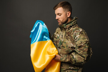 Fototapeta premium Portrait of a courageous Ukrainian military man holding the flag of Ukraine, freedom concept