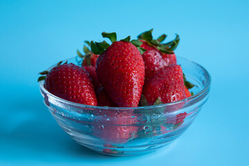 strawberries in a transparent bowl on a blue background