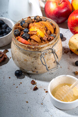 Healthy vegan dietary breakfast or snack. Apple pie overnight oatmeal, oats flakes with apples, yogurt, cinnamon, spices, blueberry. In glass, on a white marble table. Copy space