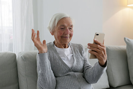 Touching image of a happy elderly woman having a fun video call with her grandchildren. Senior lady holding a phone smiling at the front facing camera. Background, close up, copy space.