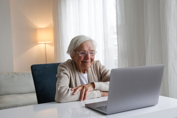 Portrait of elderly woman in eyeglasses having a video call on her laptop. Seniors and technology concept. Woman in her mid 80s using a computer. Close up, copy space, background.