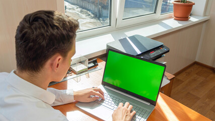 Rear view of a businessman using a laptop to type in the office. The layout of the green screen. The freelancer's workspace. People and technology. Copyspace and product placement. High quality photo