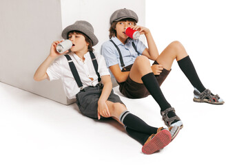 Cheerful little boys, stylish kids wearing retro clothes tasting lemonade isolated over white background. Concept of childhood, vintage summer fashion style