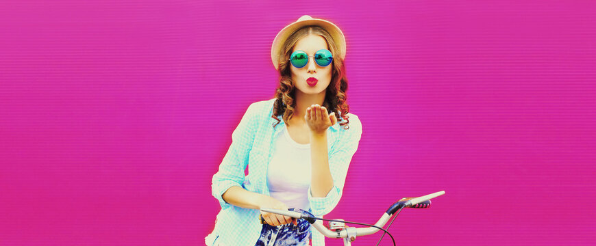 Summer colorful image of happy young woman blowing her lips with bicycle on vivid pink background