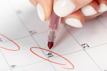 close up on employee woman hand using red pen to writing schedule on calendar 2022 to make an appointment meeting or manage timetable each day at house for work from home concept