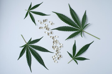Medical cannabis product. CBD oil capsules with hemp leaves on a grey background. Pharmaceutical gelatin capsules with marijuana leaves. The concept of organic food supplements
