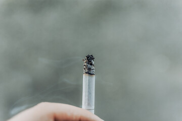Close up to a hand holding a smoking cigarette with ash. Quit smoking concept