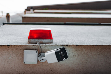 CCTV security camera mounted underneath a warning lamp at the edge of a building